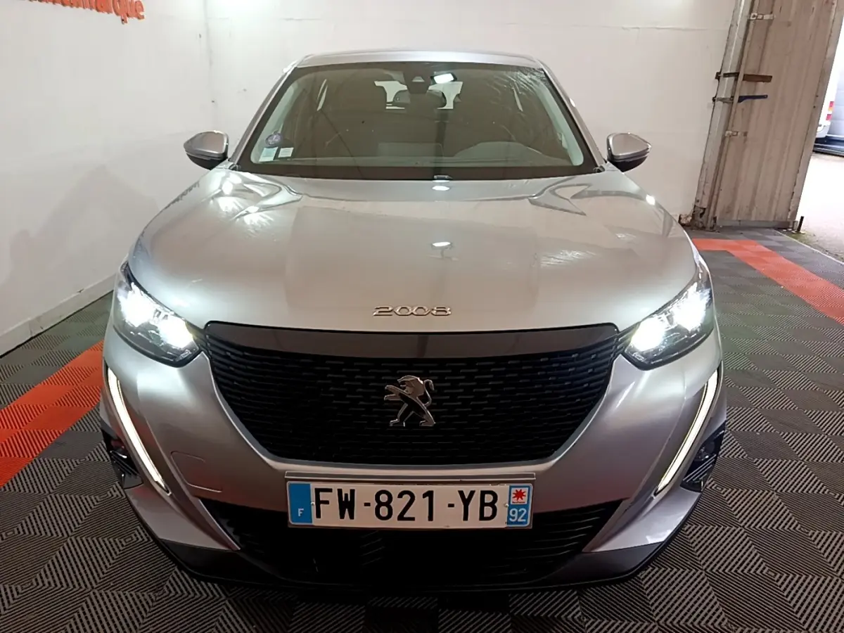 Vue frontale d’un Peugeot 2008 gris clair avec phares allumés et calandre noire distinctive.