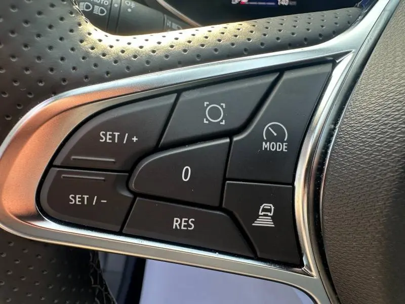 Gros plan sur les commandes au volant en cuir perforé du Renault Symbioz rouge, avec boutons de régulateur et mode conduite.