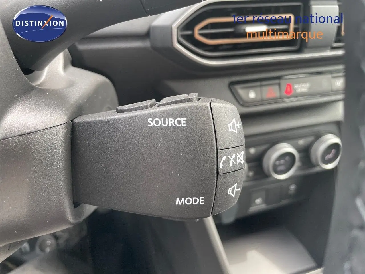 Gros plan sur la commande audio au volant de la Dacia Sandero Stepway 2024, intérieur noir avec commandes climatisation en arrière-plan.