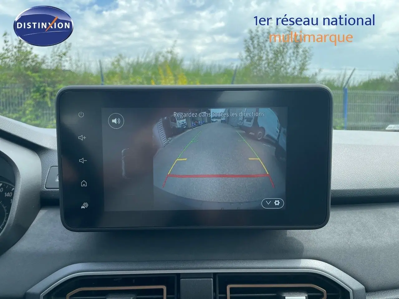 Écran central de la Dacia Sandero Stepway 2024 montrant la caméra de recul avec vue arrière sur un parking extérieur.