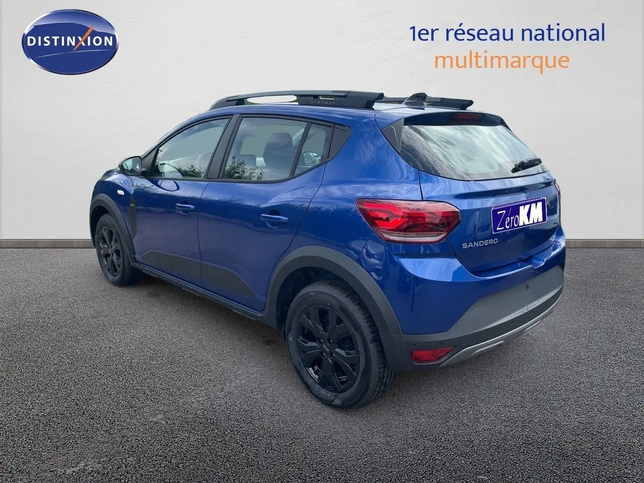 Vue 3/4 arrière côté gauche d'une Dacia Sandero Stepway 2024 bleu Iron Metal avec jantes noires et barres de toit.