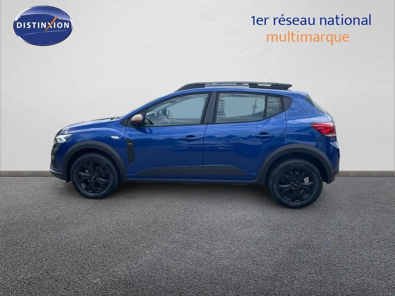 Profil côté gauche d'une Dacia Sandero Stepway 2024 bleu iron metal avec jantes noires et barres de toit.