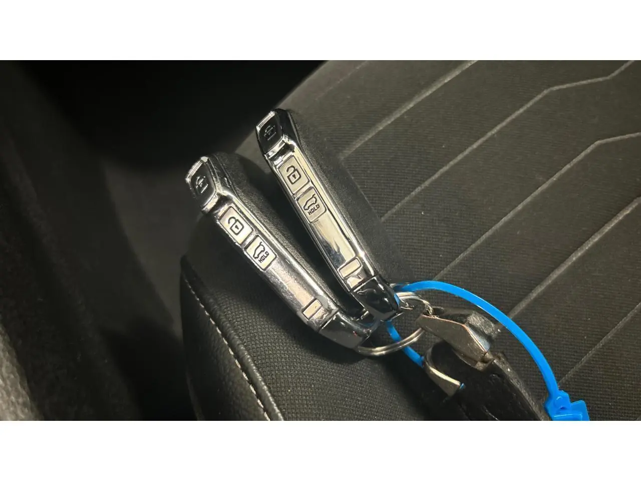 Gros plan sur deux clés de voiture KIA posées sur un siège en tissu noir à coutures blanches.