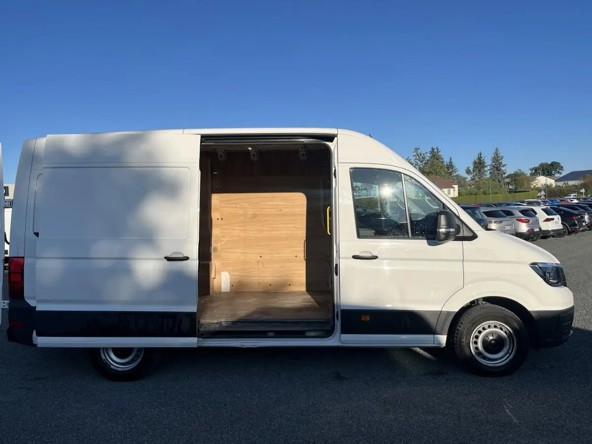 Vue latérale droite d'un Volkswagen Crafter blanc avec porte coulissante ouverte révélant l'espace de chargement en bois.