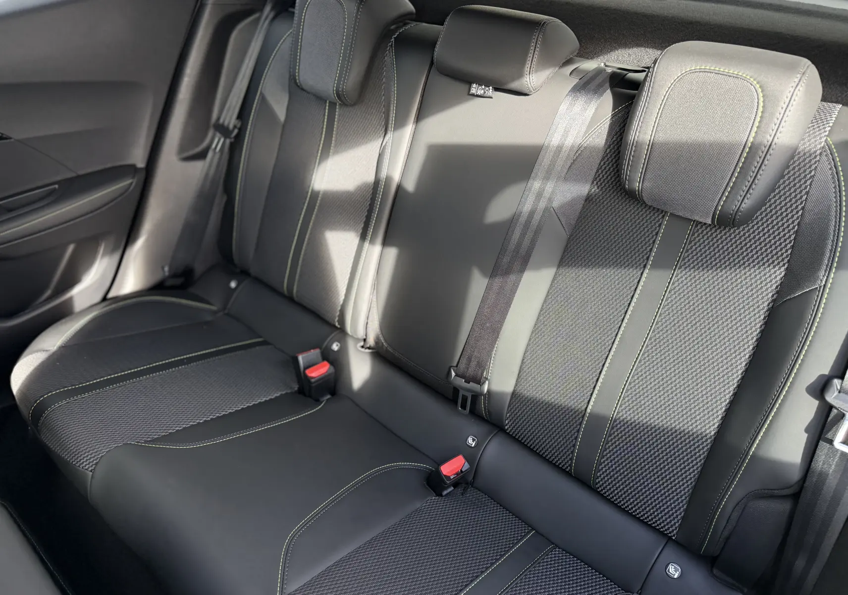 Vue intérieure des sièges arrière en cuir noir et tissu avec surpiqûres vertes du Peugeot 2008 Hybrid 145ch GT 2025.