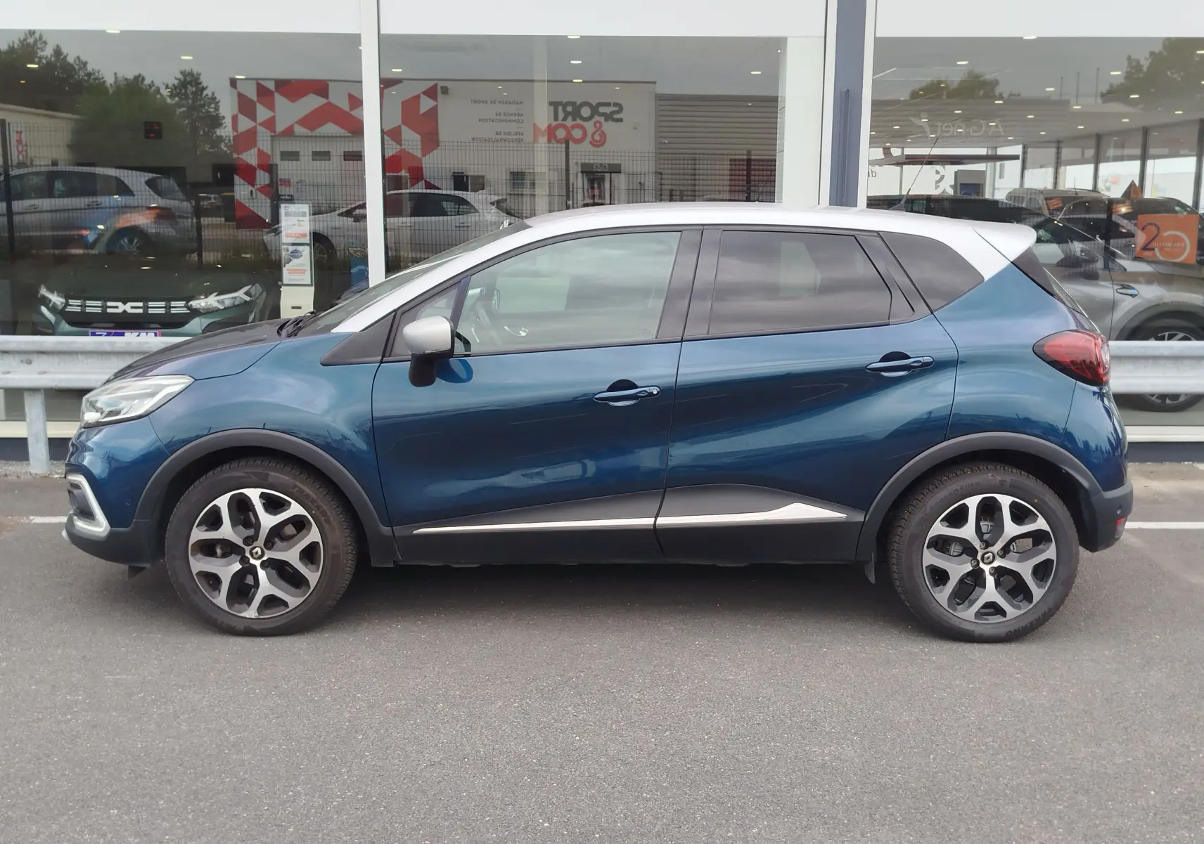 Profil droit d’un Renault Captur 2018 bleu marine fumé avec toit gris platine et jantes bi-ton, garé devant une vitrine.