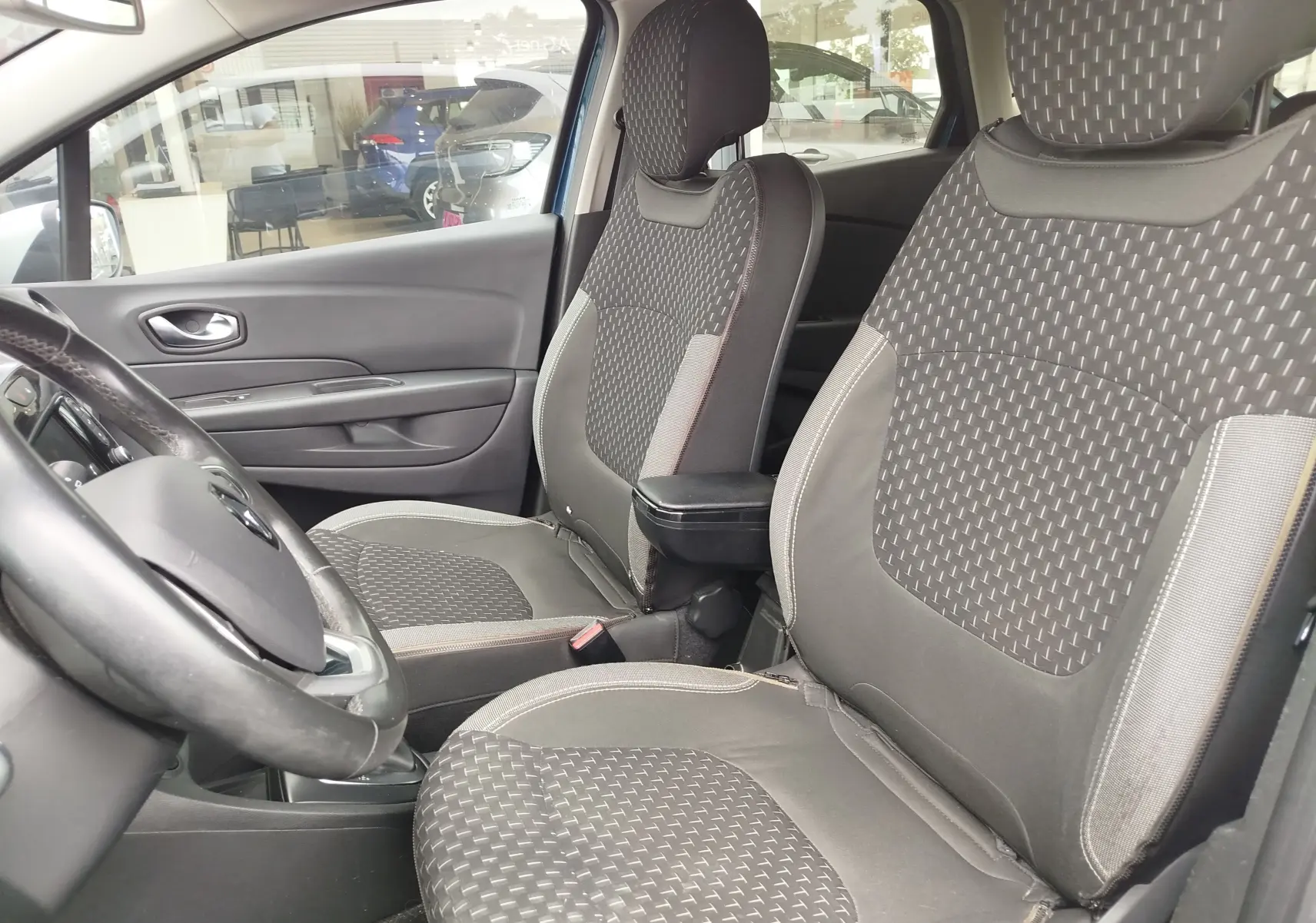 Vue intérieure côté conducteur du Renault Captur 2018, sièges tissu gris à motifs géométriques et accoudoir central.