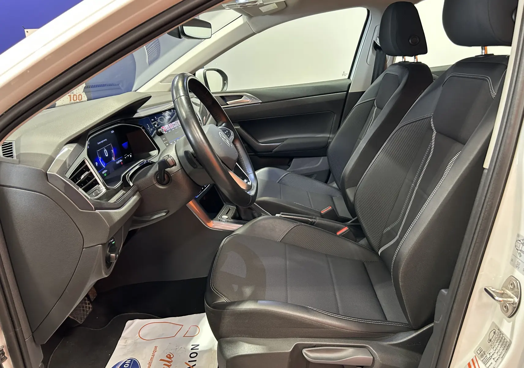 Intérieur avant droit du Volkswagen Taigo blanc 2022, sièges noirs avec surpiqûres blanches et tableau de bord numérique.