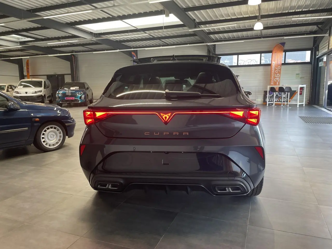Vue arrière d'une CUPRA Leon gris magnétique avec feux arrière en bandeau lumineux Tri-LED et double sortie d'échappement noire.