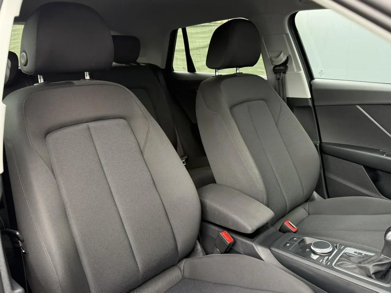 Intérieur de l'Audi Q2 35 TFSI 2023 montrant les sièges avant gris foncé et la console centrale avec commandes S-Line.