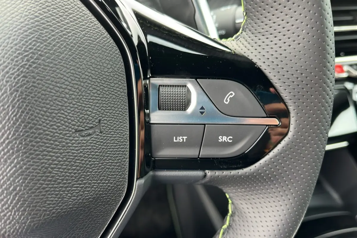 Gros plan sur les commandes gauche du volant perforé du Peugeot 2008 Hybrid 145 GT Vision 2025, finition noire.