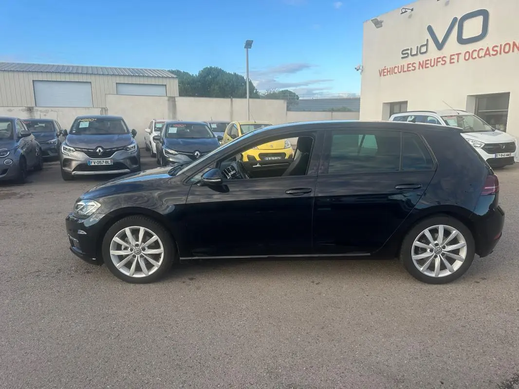 Profil côté gauche d'une Volkswagen Golf noire 2018 avec jantes alliage 17 pouces, stationnée en extérieur sur un parking.