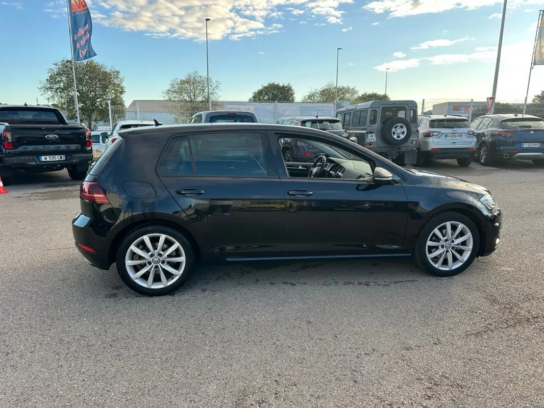 Profil côté gauche d'une Volkswagen Golf noire de 2018 avec jantes alliage 17 pouces sur parking extérieur.