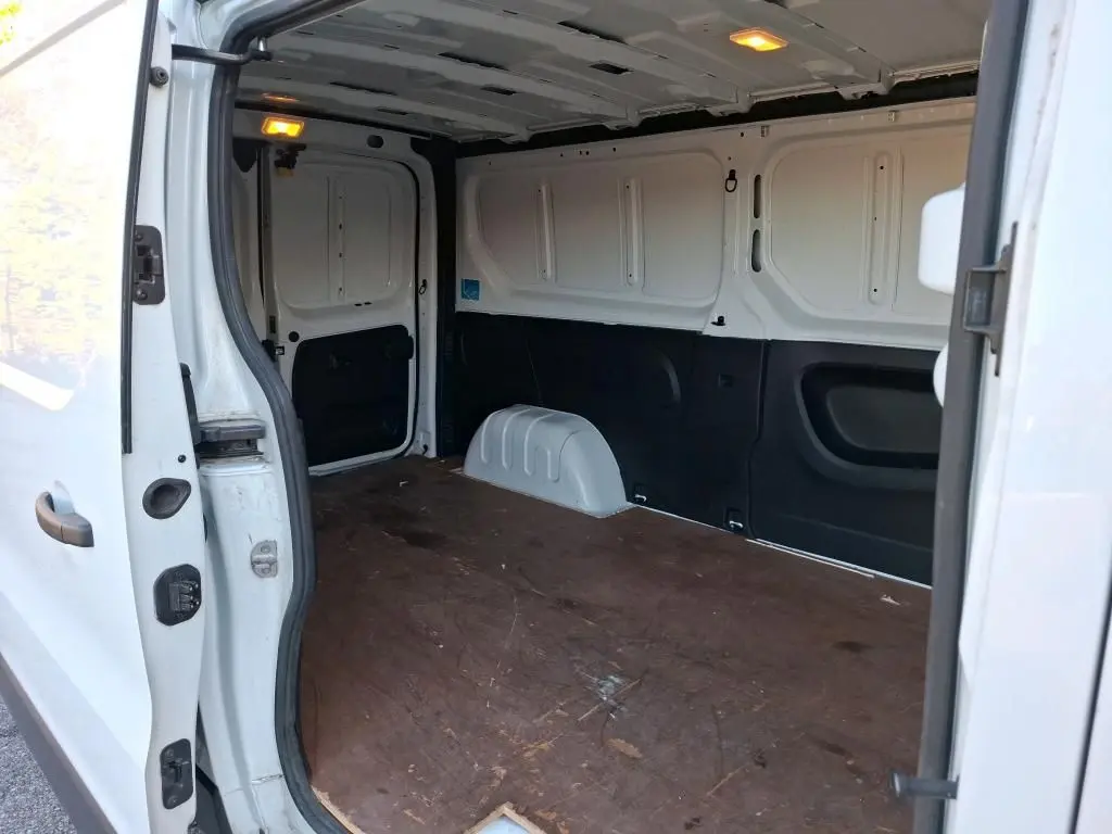 Vue intérieure du fourgon blanc Renault Trafic L2H1 2019, montrant l'espace de chargement avec plancher en bois et éclairage allumé.