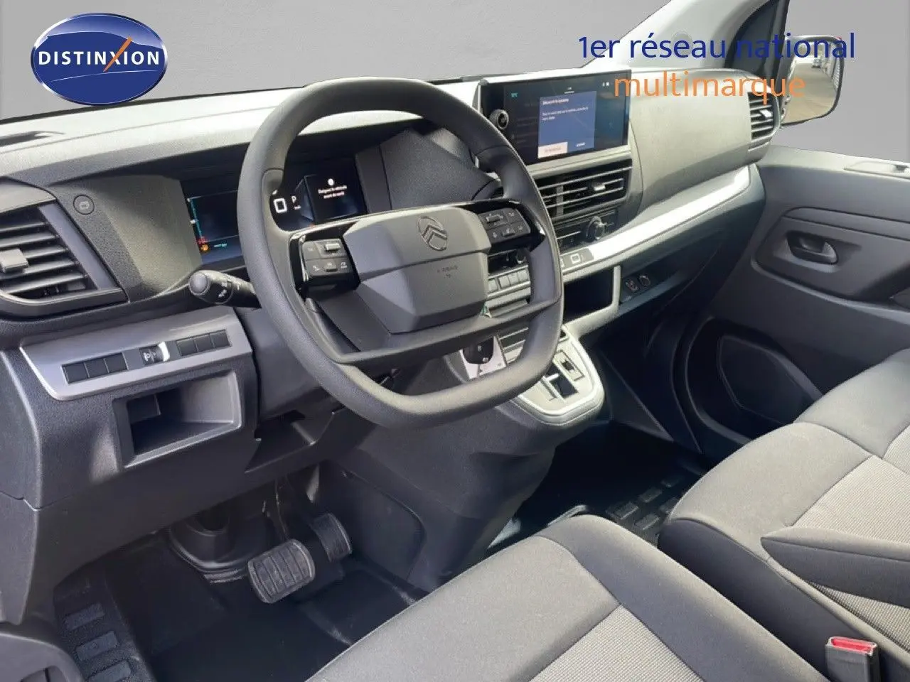 Vue intérieure côté conducteur du Citroën Jumpy gris titane, montrant le volant, tableau de bord et sièges en tissu noir.