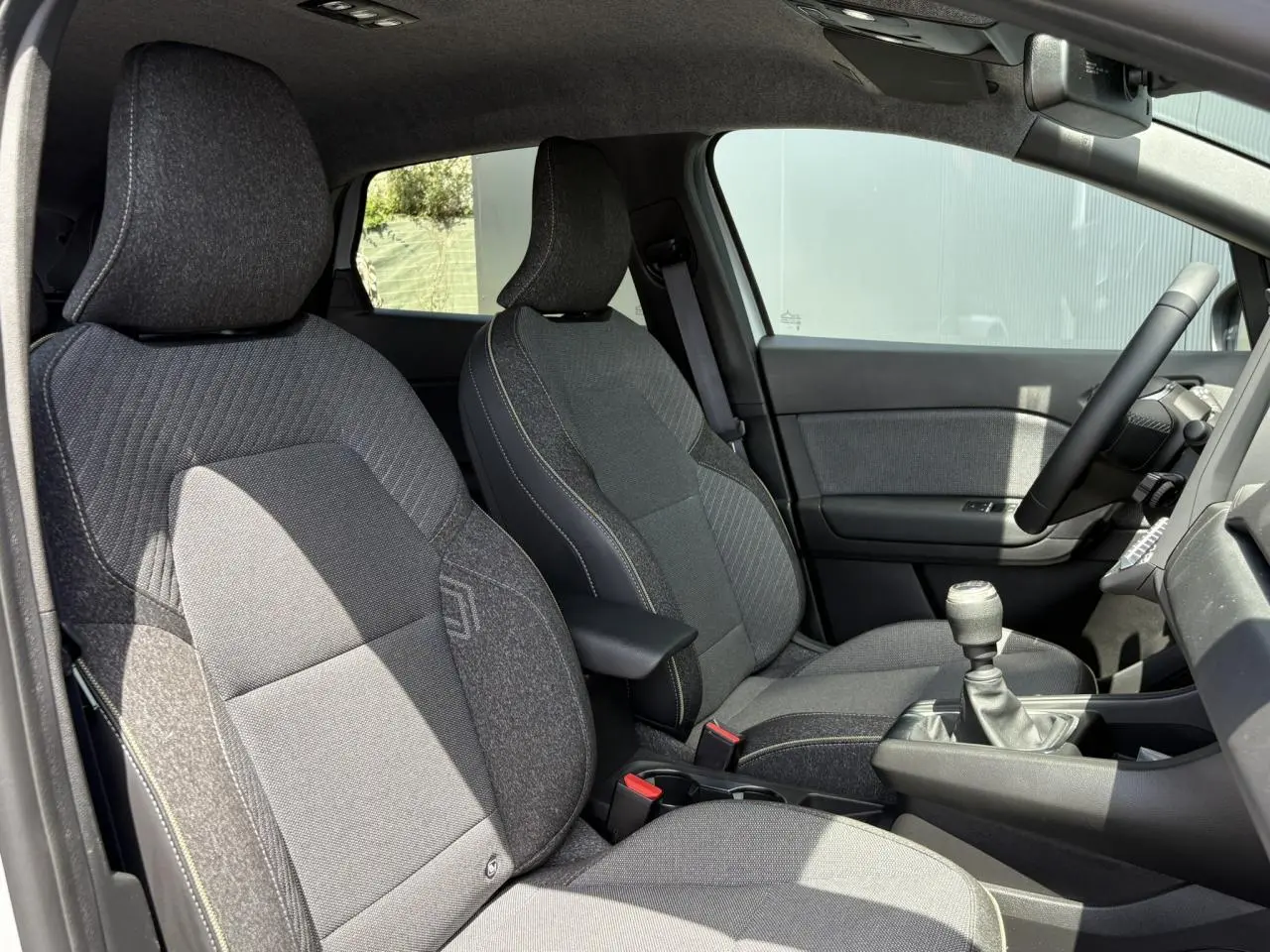 Vue intérieure côté conducteur du Renault Captur TCE 90 Techno 2025, sièges tissu gris avec surpiqûres contrastées.