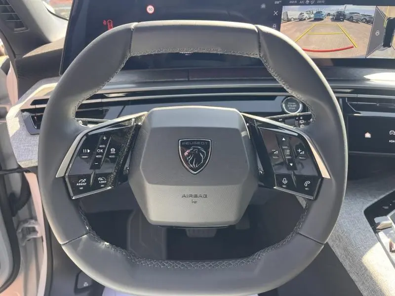 Vue rapprochée du volant cuir multifonction du Peugeot 5008 blanc Okénite, avec écran tactile et caméra de recul visible.