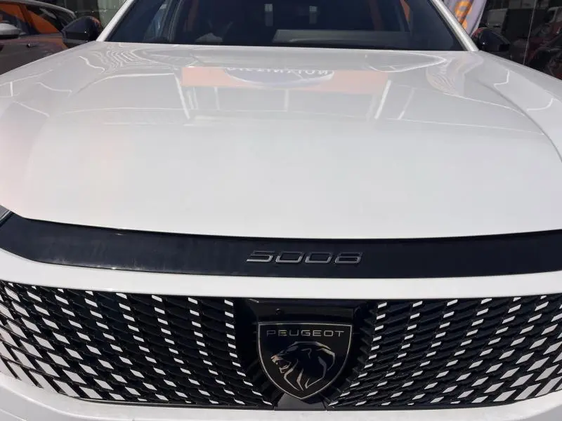 Vue frontale rapprochée du Peugeot 5008 blanc Okénite avec calandre noire et logo lion distinctif.