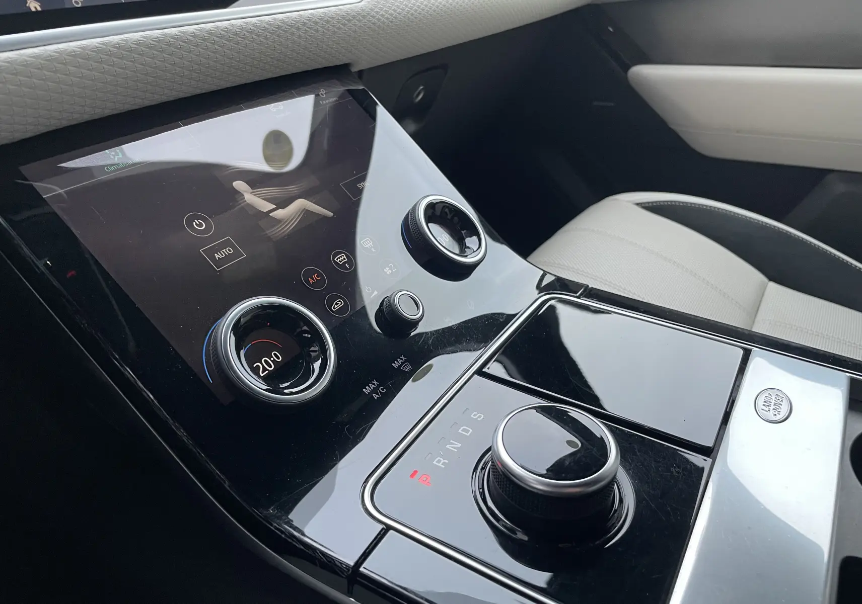 Gros plan sur la console centrale noire brillante du Range Rover Velar 2018 avec commandes tactiles et siège beige visible.