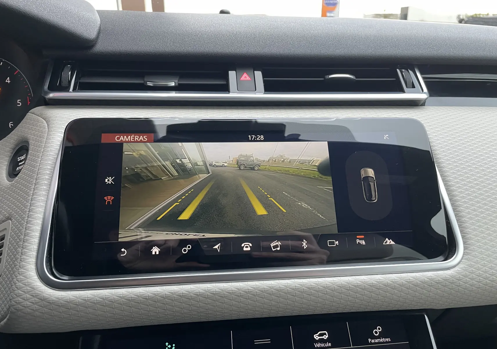 Écran central du Range Rover Velar D300 montrant la caméra de recul avec lignes de guidage jaunes sur route grise.