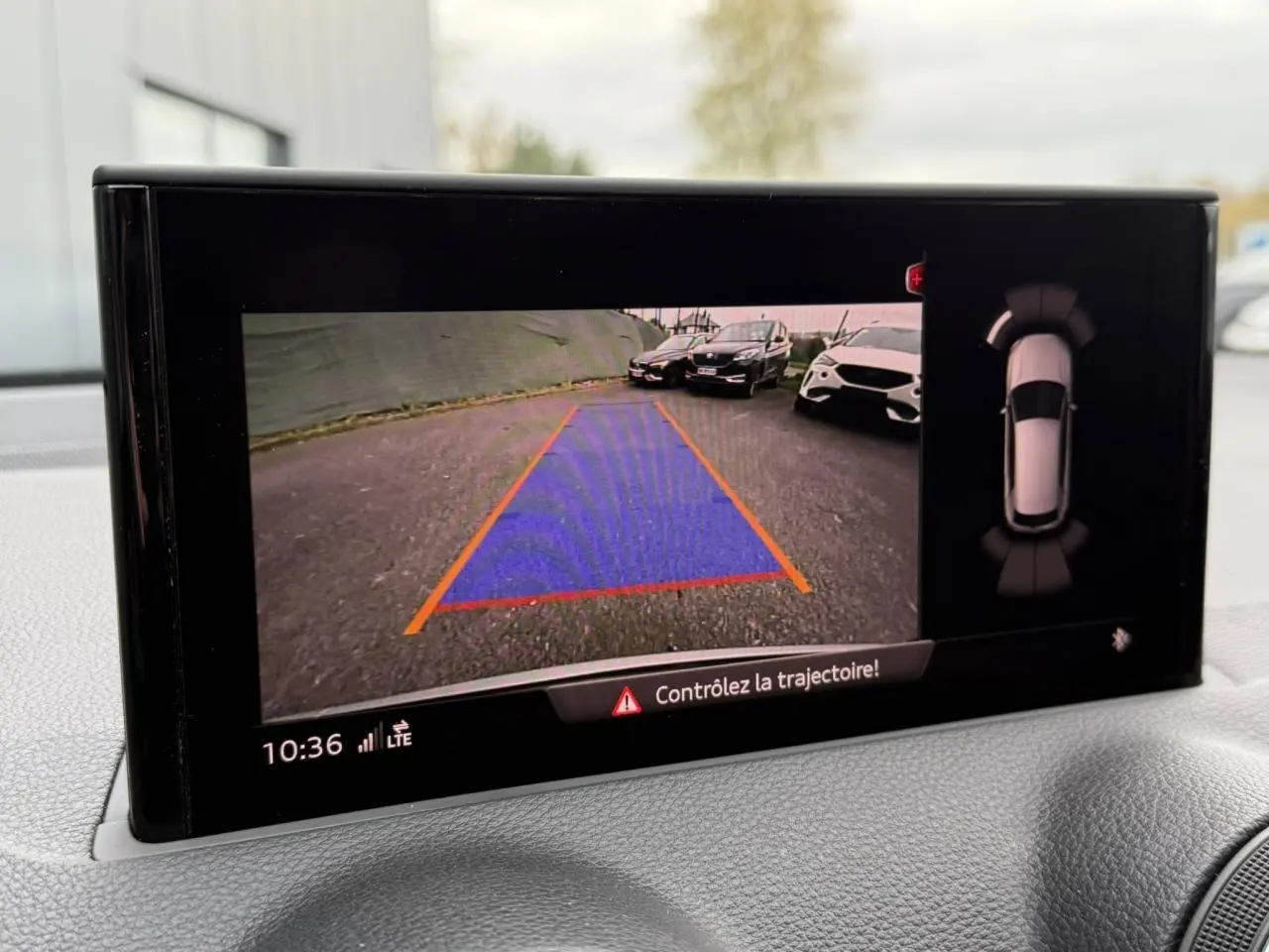 Écran de caméra de recul de l'Audi Q2 noir Mythe montrant la zone de stationnement et l'alerte trajectoire.
