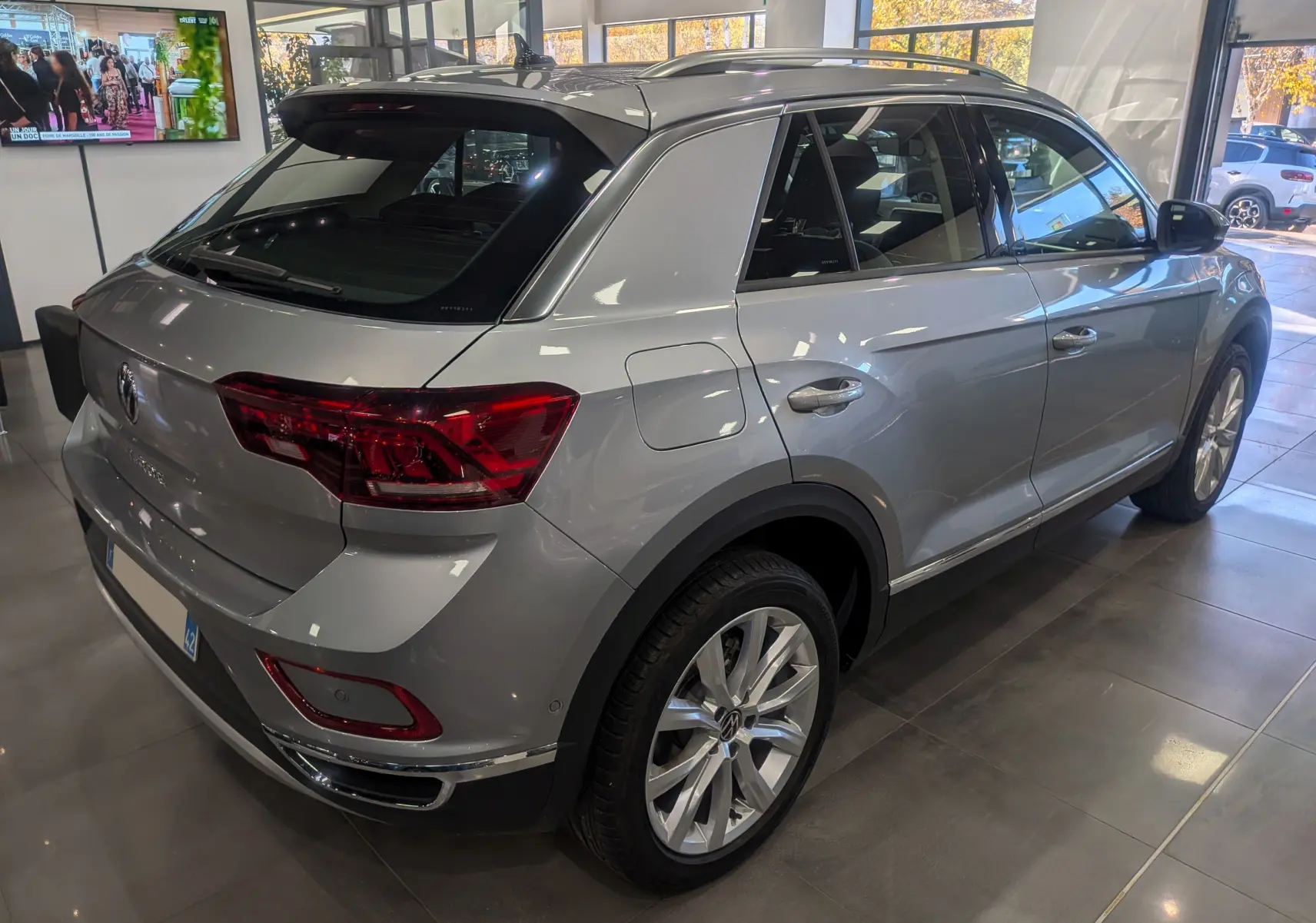 Volkswagen T-Roc gris pyrite vu en 3/4 arrière droit, avec jantes alliage et feux arrière LED en showroom.