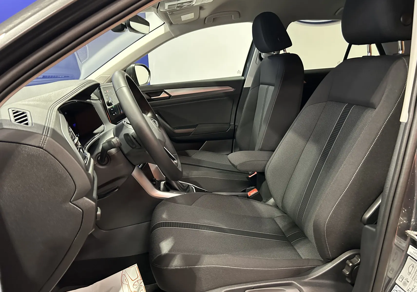 Vue intérieure côté conducteur du Volkswagen T-Roc 2025, sièges tissu noir avec coutures contrastées et tableau de bord moderne.