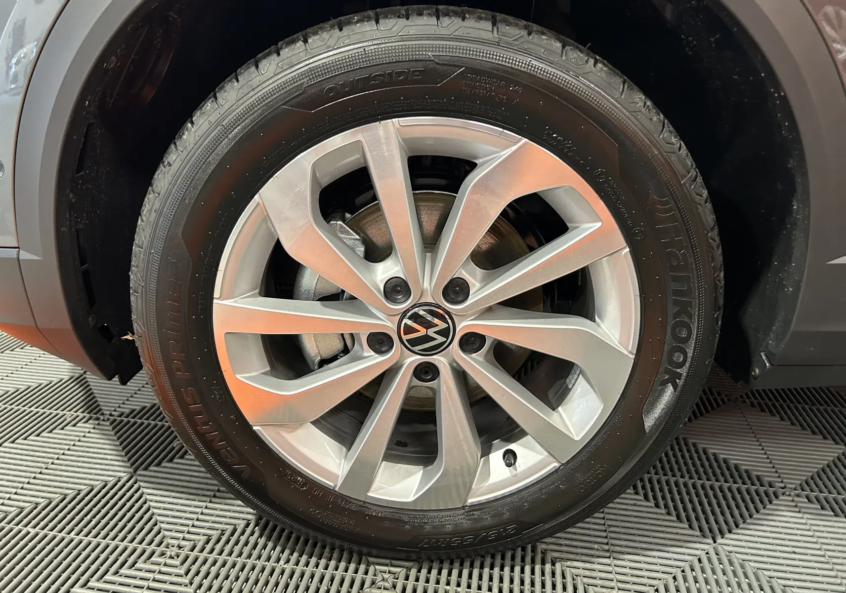 Gros plan sur la jante alliage argentée avec logo Volkswagen d’un Volkswagen T-Roc gris Indium métal.