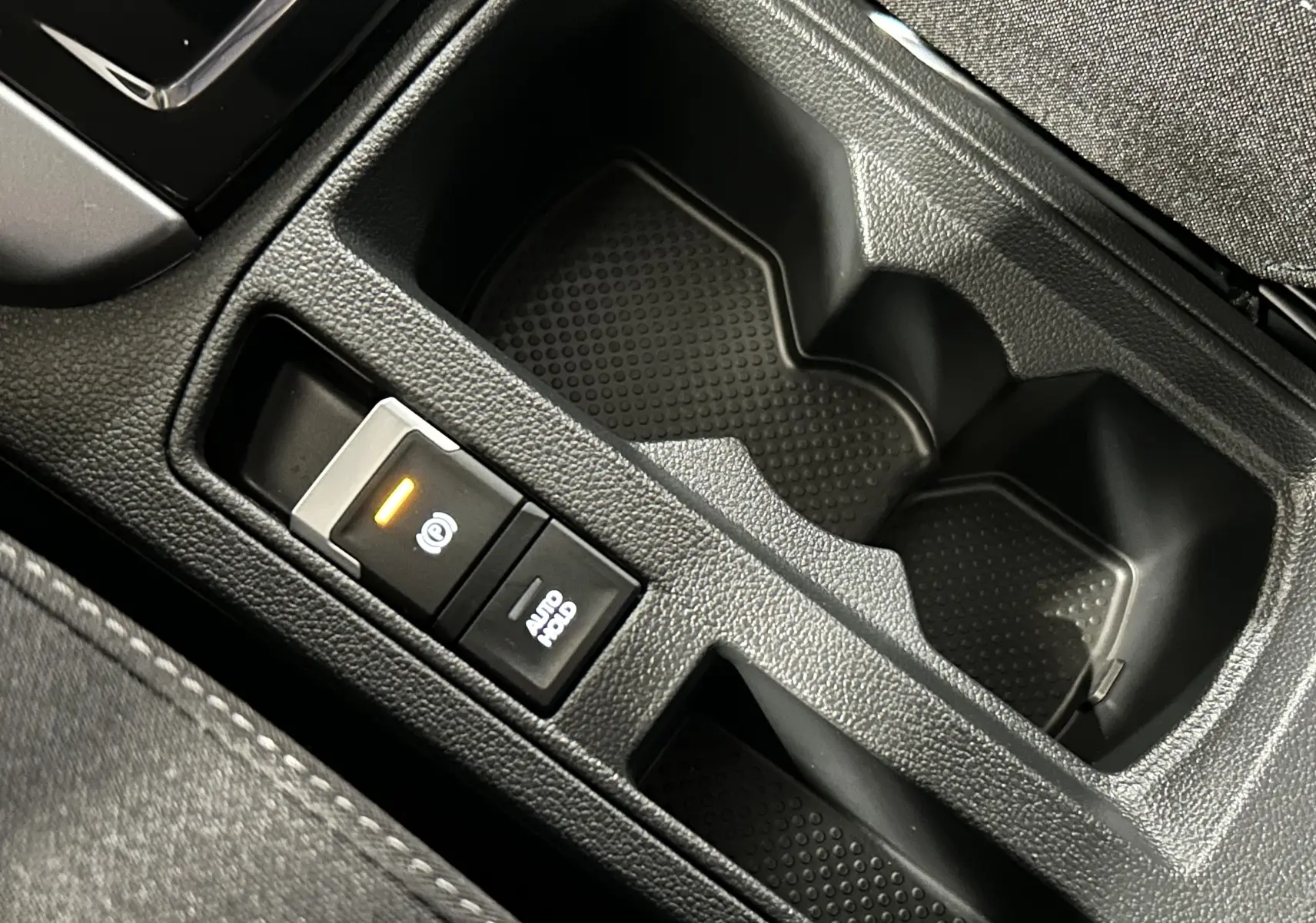 Gros plan sur la console centrale noire du Volkswagen T-Roc 2025, avec bouton frein à main électronique et porte-gobelets.