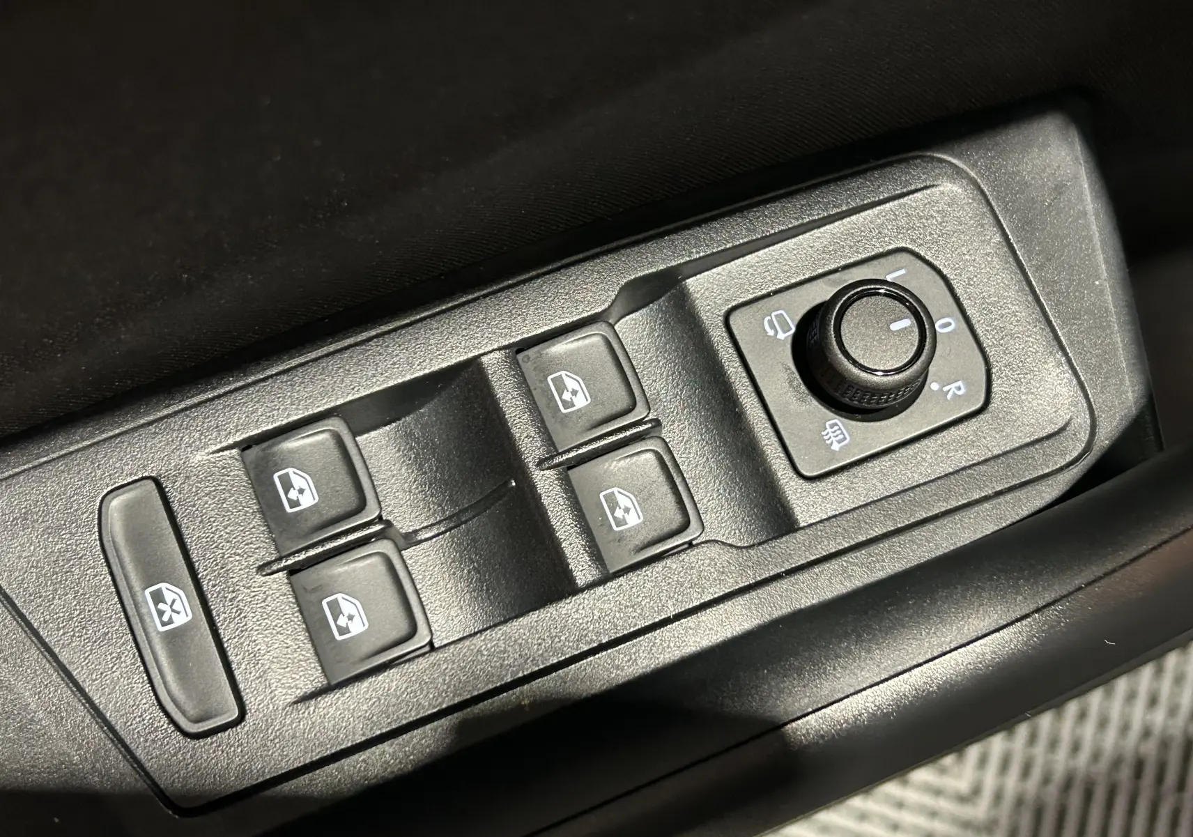 Gros plan sur les commandes des vitres et rétroviseurs électriques côté conducteur du Volkswagen T-Roc gris Indium 2025.