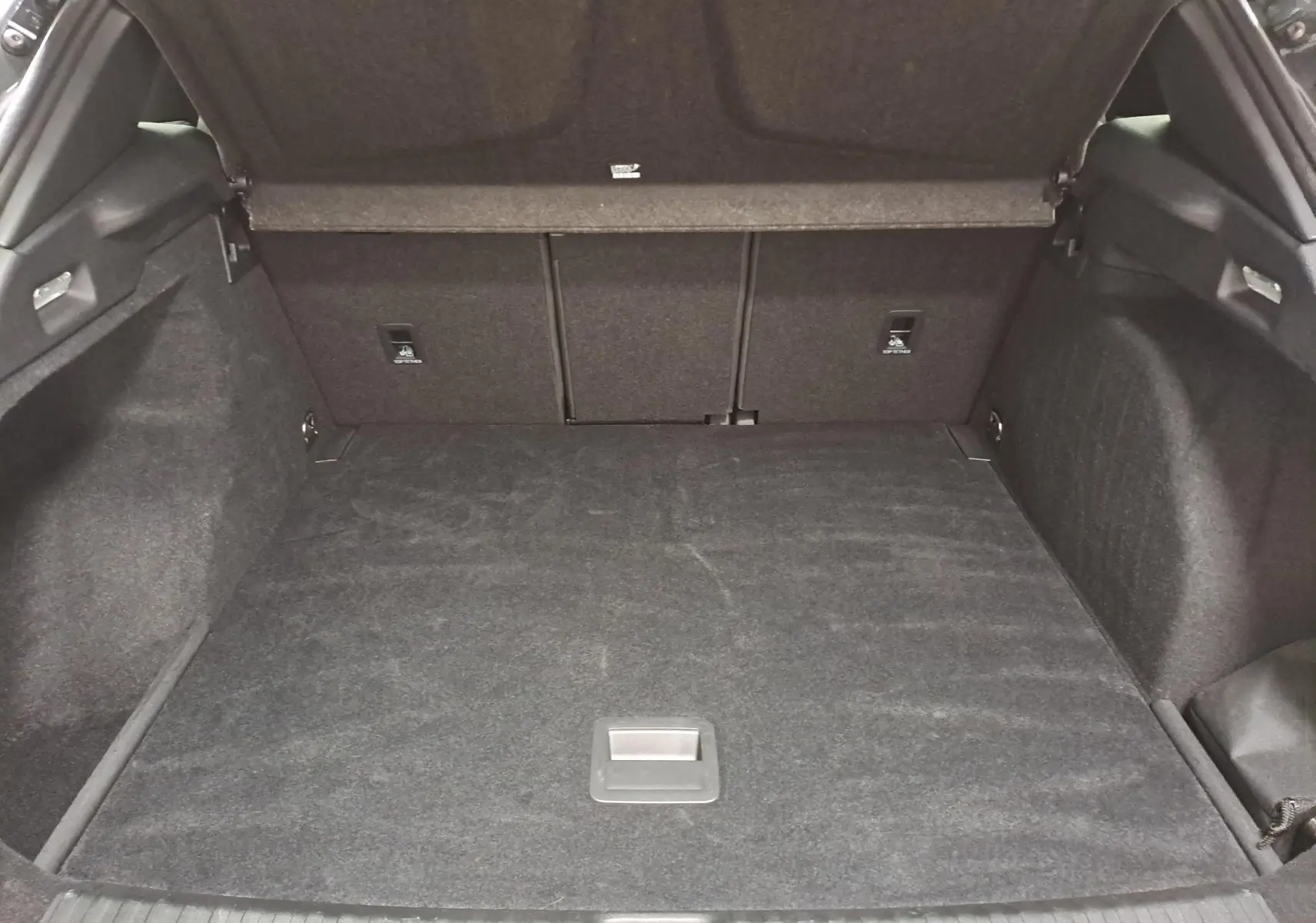 Coffre ouvert vu de l'arrière d'une CUPRA TERRAMAR 1.5 eTSI gris Timanfaya, espace de chargement vide et tapis noir.