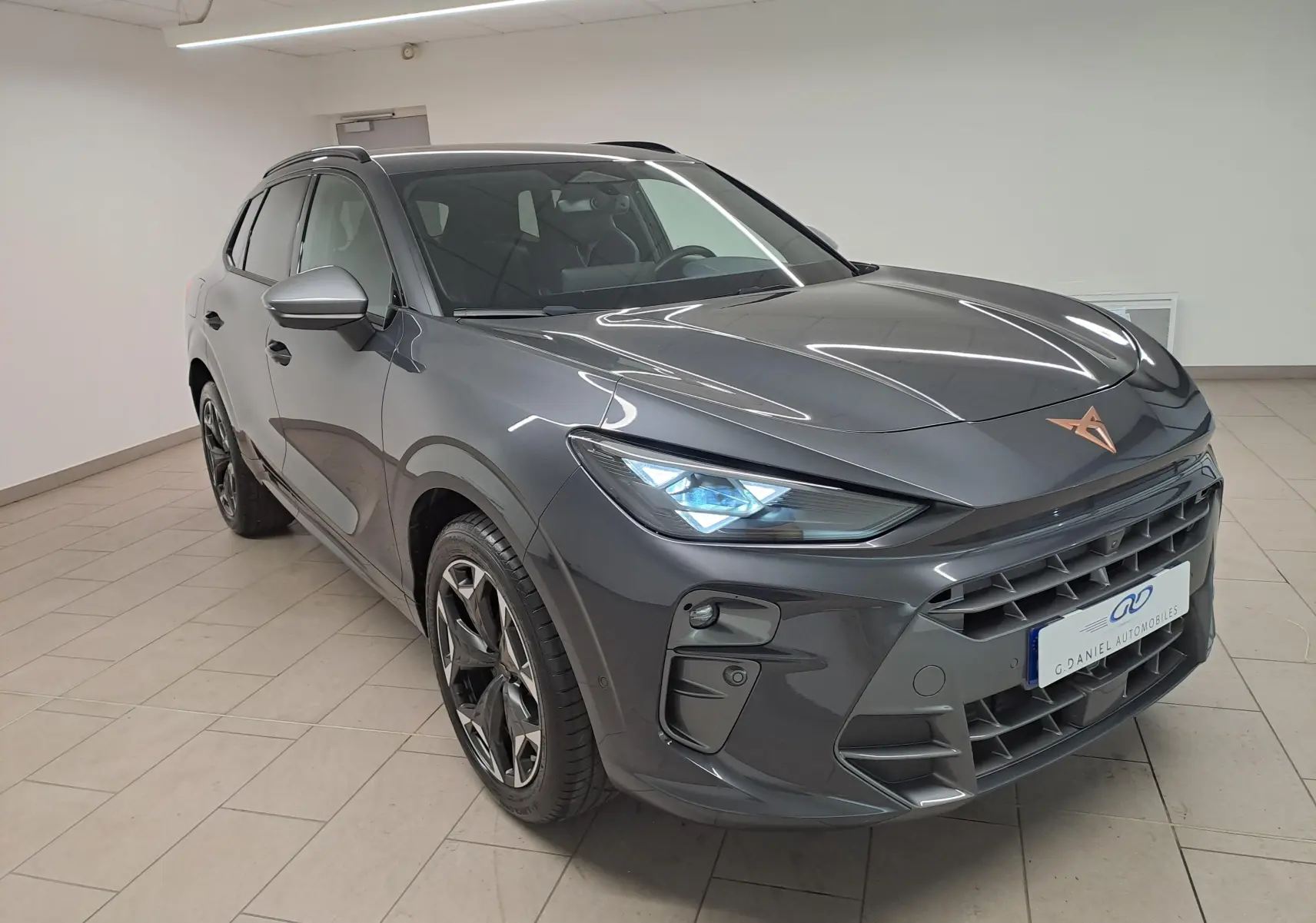 Vue 3/4 avant droite d'une CUPRA TERRAMAR 2025 gris Timanfaya avec jantes 19'' Cosmic usinées et feux allumés.