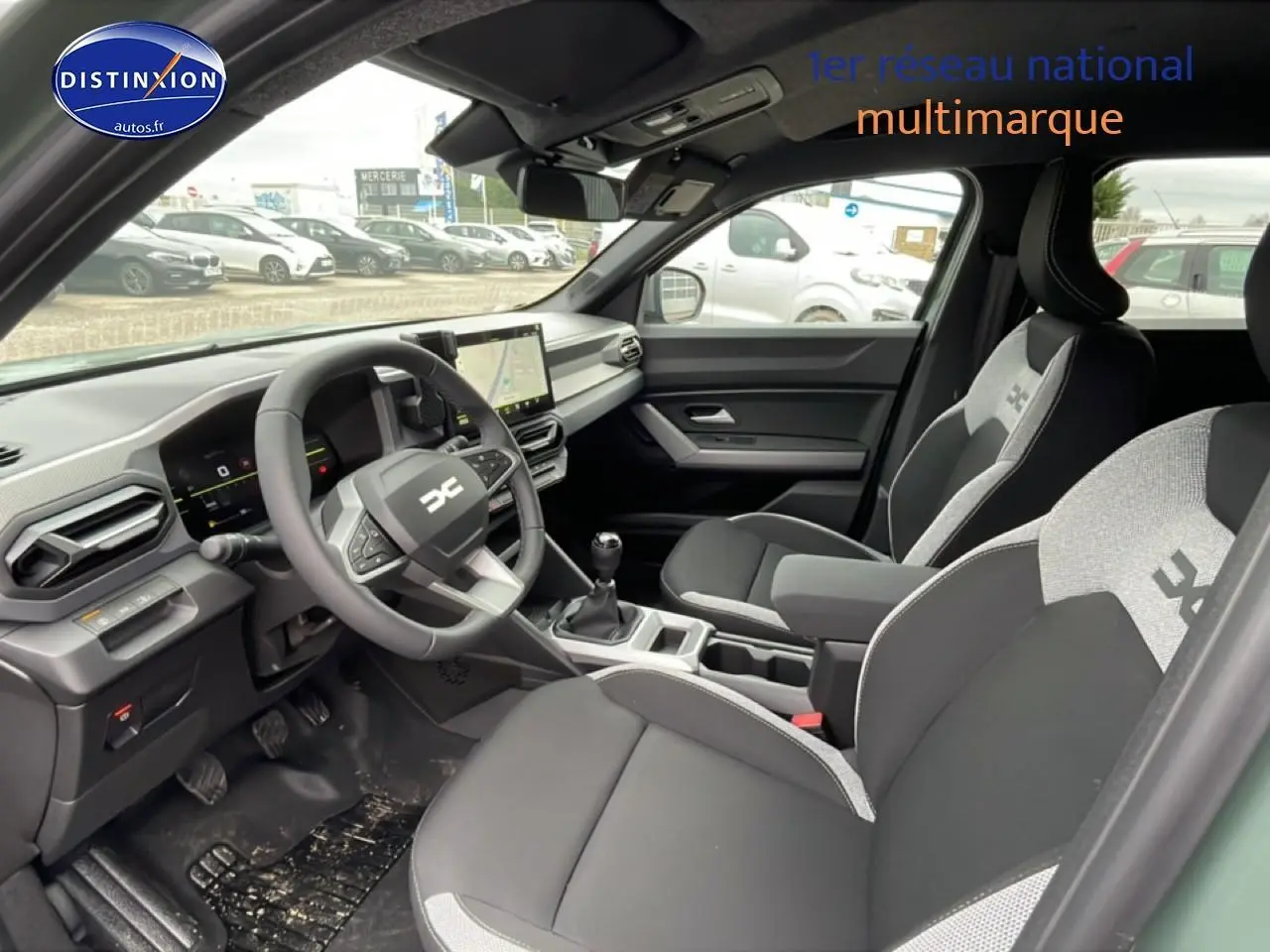 Vue intérieure côté conducteur du Dacia Duster 2026 vert kaki, avec tableau de bord numérique et sièges bi-ton gris et noir.