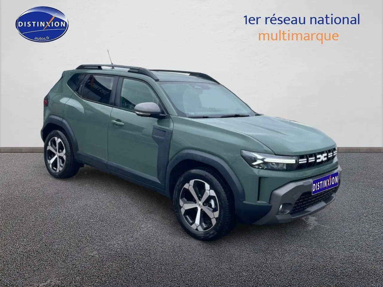 Dacia Duster vert kaki en 3/4 avant droit, avec jantes alu et barres de toit noires visibles.