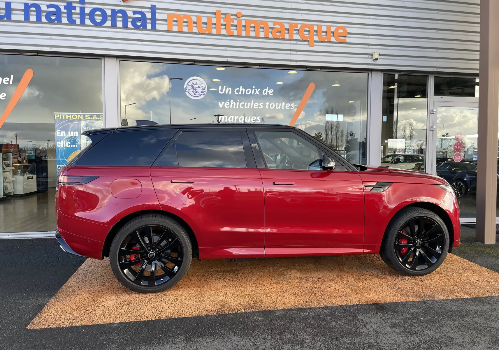 Vue de profil côté gauche d’un Range Rover Sport P440 HSE R-Dynamic rouge Italian Racing avec jantes noires 23 pouces et toit noir.
