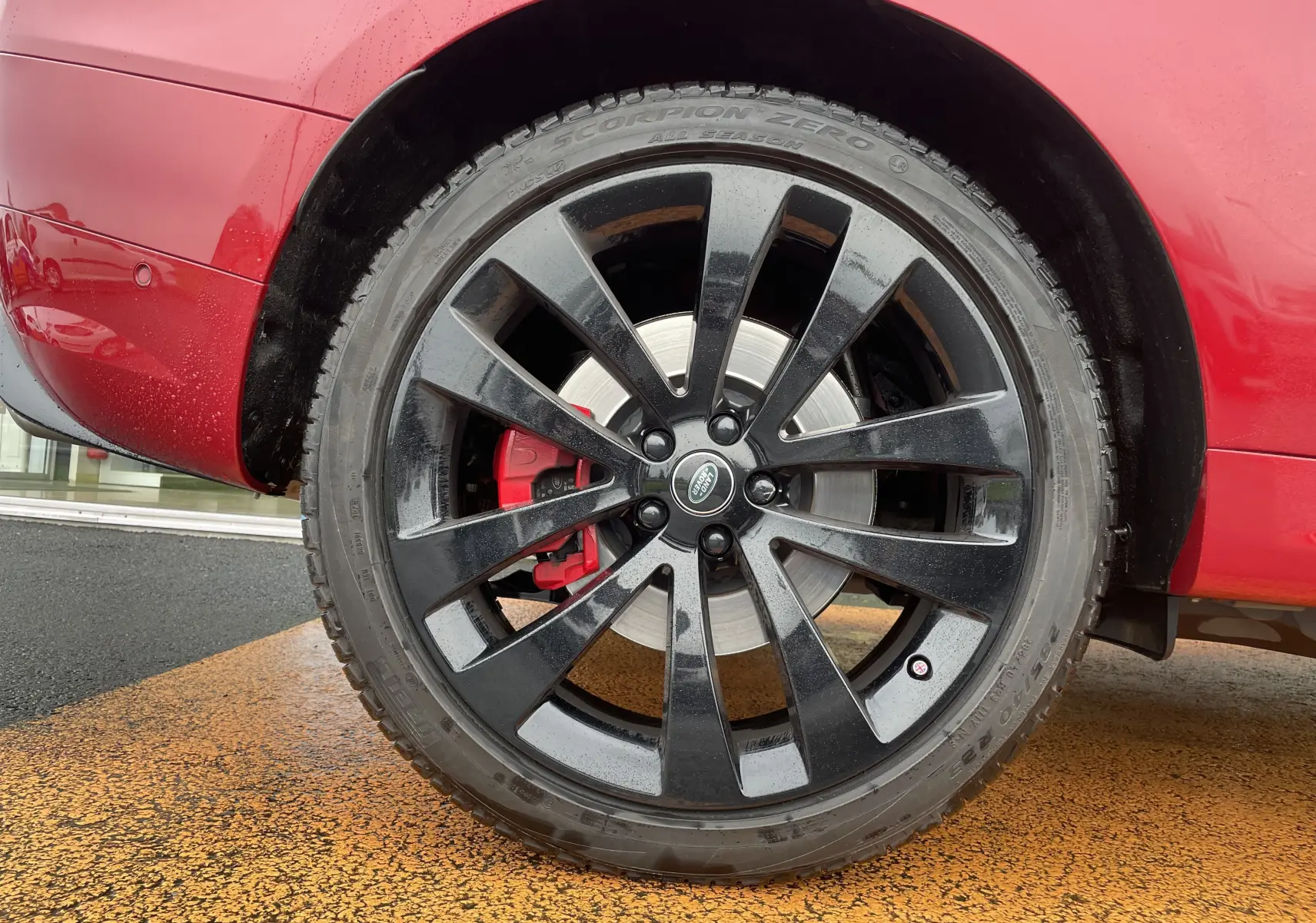 Gros plan sur la roue arrière droite noire avec étrier de frein rouge du Range Rover Sport P440 HSE R-Dynamic rouge italien.