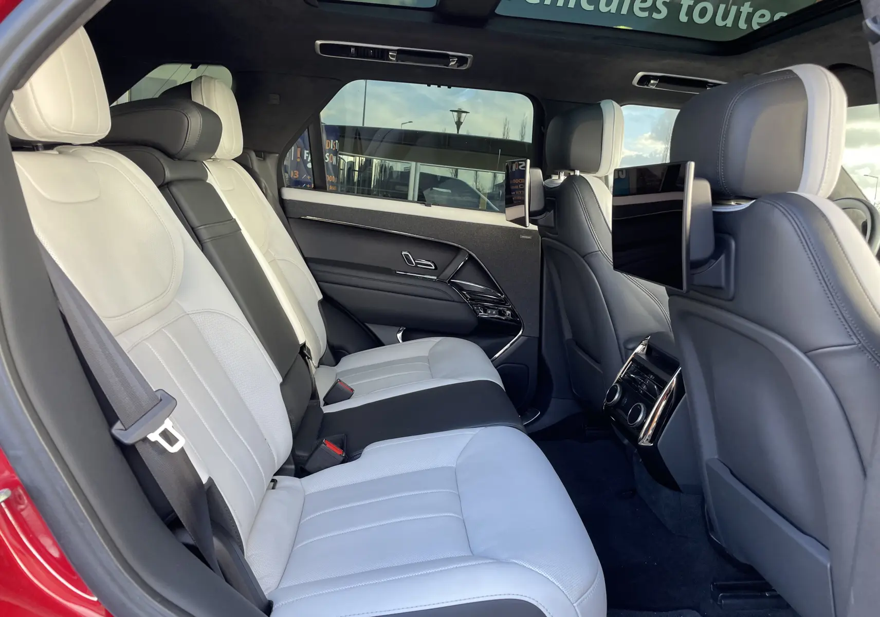 Vue intérieure arrière côté gauche du Range Rover Sport P440 HSE R-Dynamic 2023, sièges cuir blanc avec écrans intégrés aux appuie-têtes.