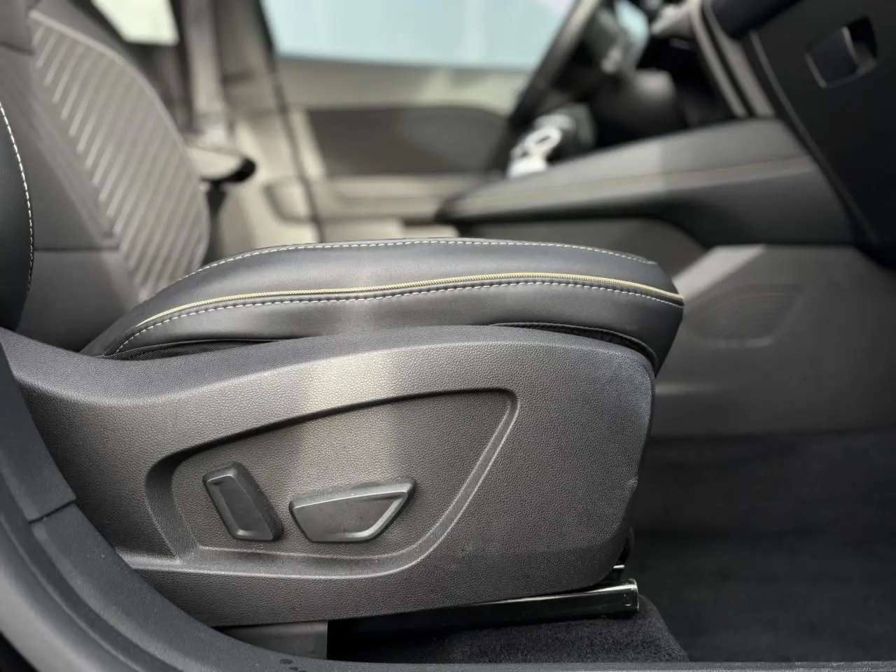 Gros plan sur le réglage électrique du siège conducteur noir avec surpiqûres beiges dans l’habitacle Renault Symbioz.