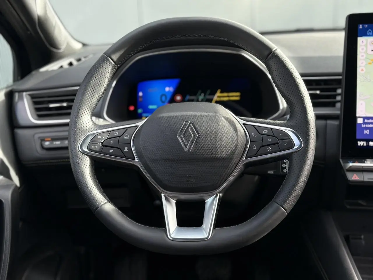 Volant en cuir noir perforé de Renault SYMBIOZ 2025 vu de face avec tableau de bord numérique en arrière-plan.