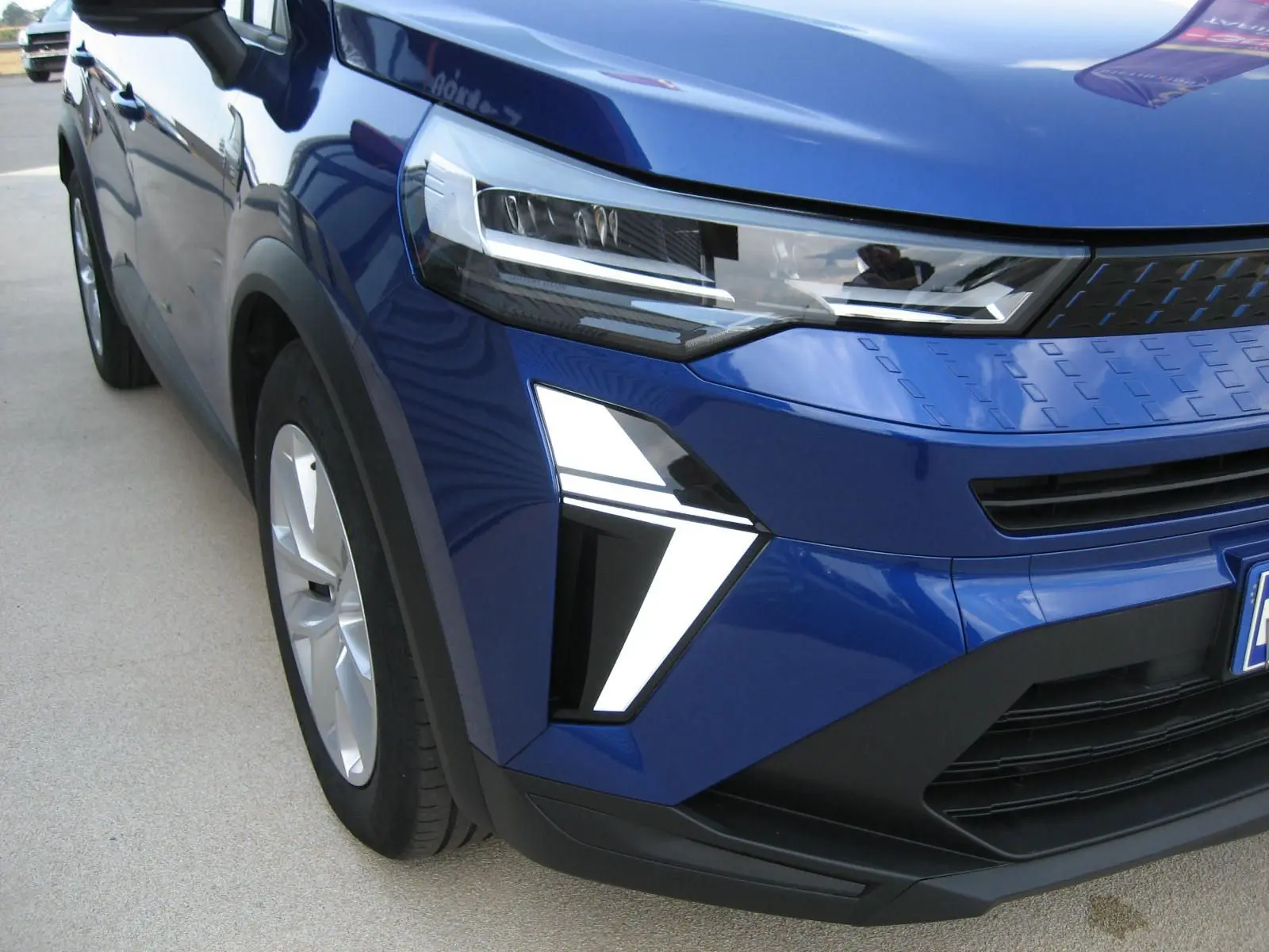 Vue 3/4 avant droit du Renault Captur II bleu iron, mettant en valeur ses phares LED et la calandre moderne.