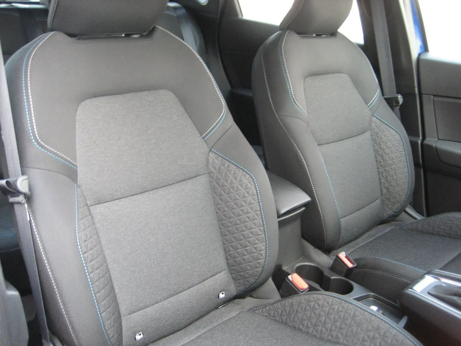 Vue rapprochée des sièges avant gris foncé avec surpiqûres bleues du Renault Captur II 1.6 E-TECH Hybride 2025.