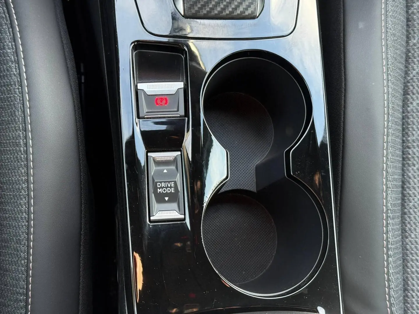 Gros plan sur la console centrale noire brillante avec bouton Drive Mode et frein à main électrique du Peugeot e-2008.
