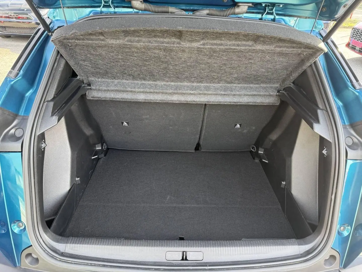 Coffre ouvert vu de l'arrière du Peugeot e-2008 bleu Obsession, montrant l'espace de rangement vide.