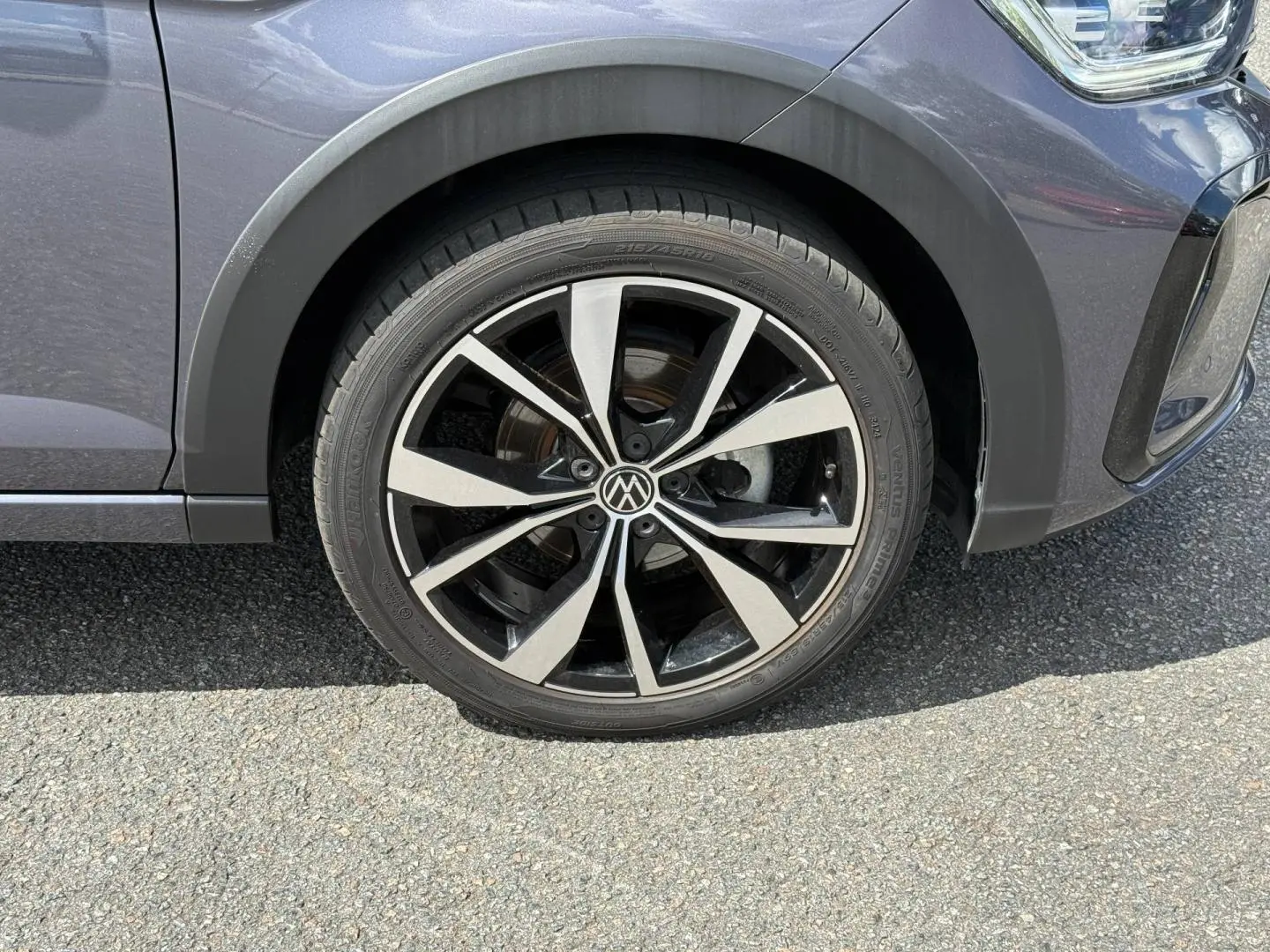 Gros plan sur la roue avant droite du Volkswagen Taigo gris avec jante alliage bicolore et logo VW central.