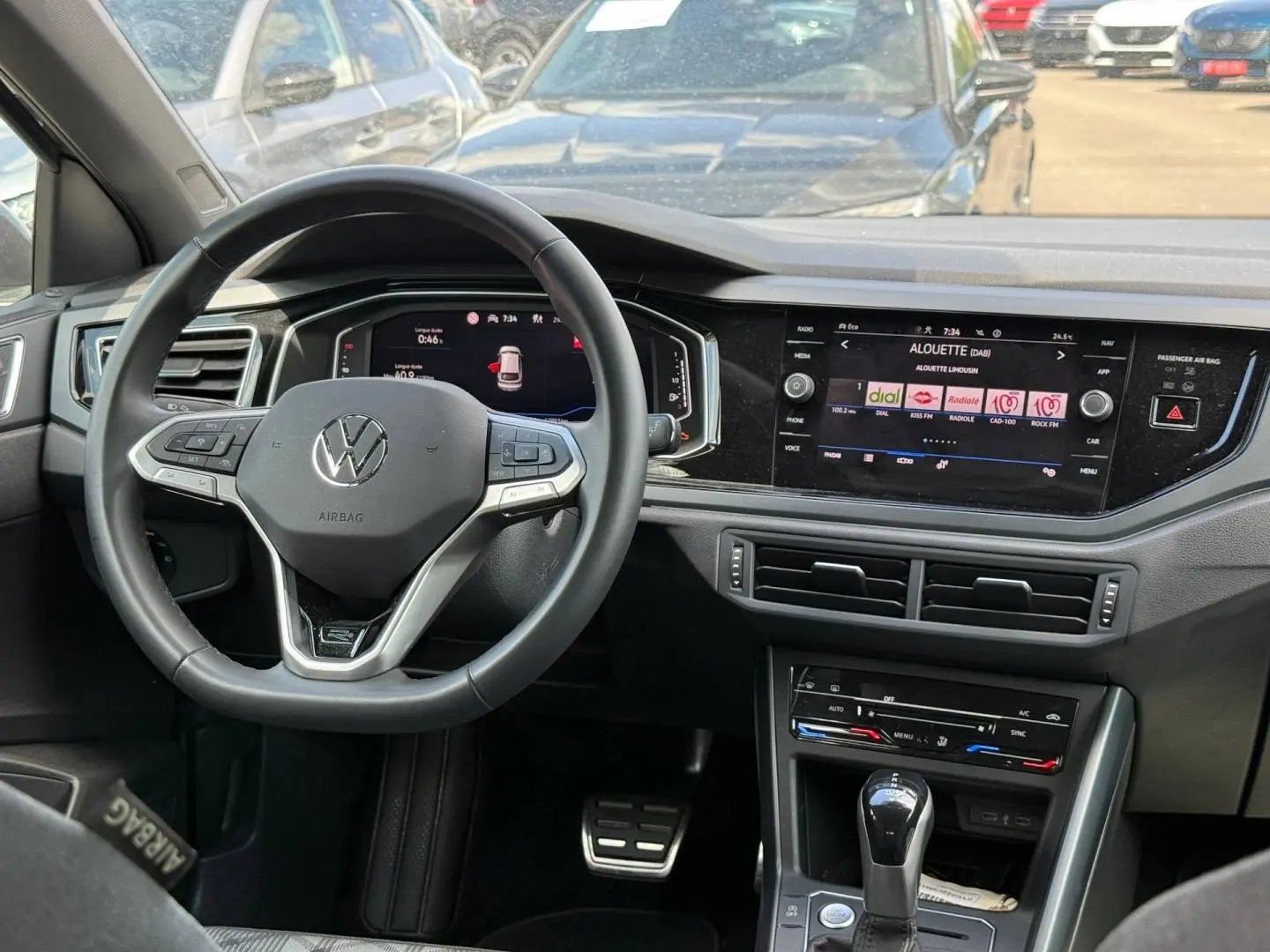 Vue intérieure frontale du tableau de bord du Volkswagen Taigo gris avec volant multifonction et écran tactile central allumé.
