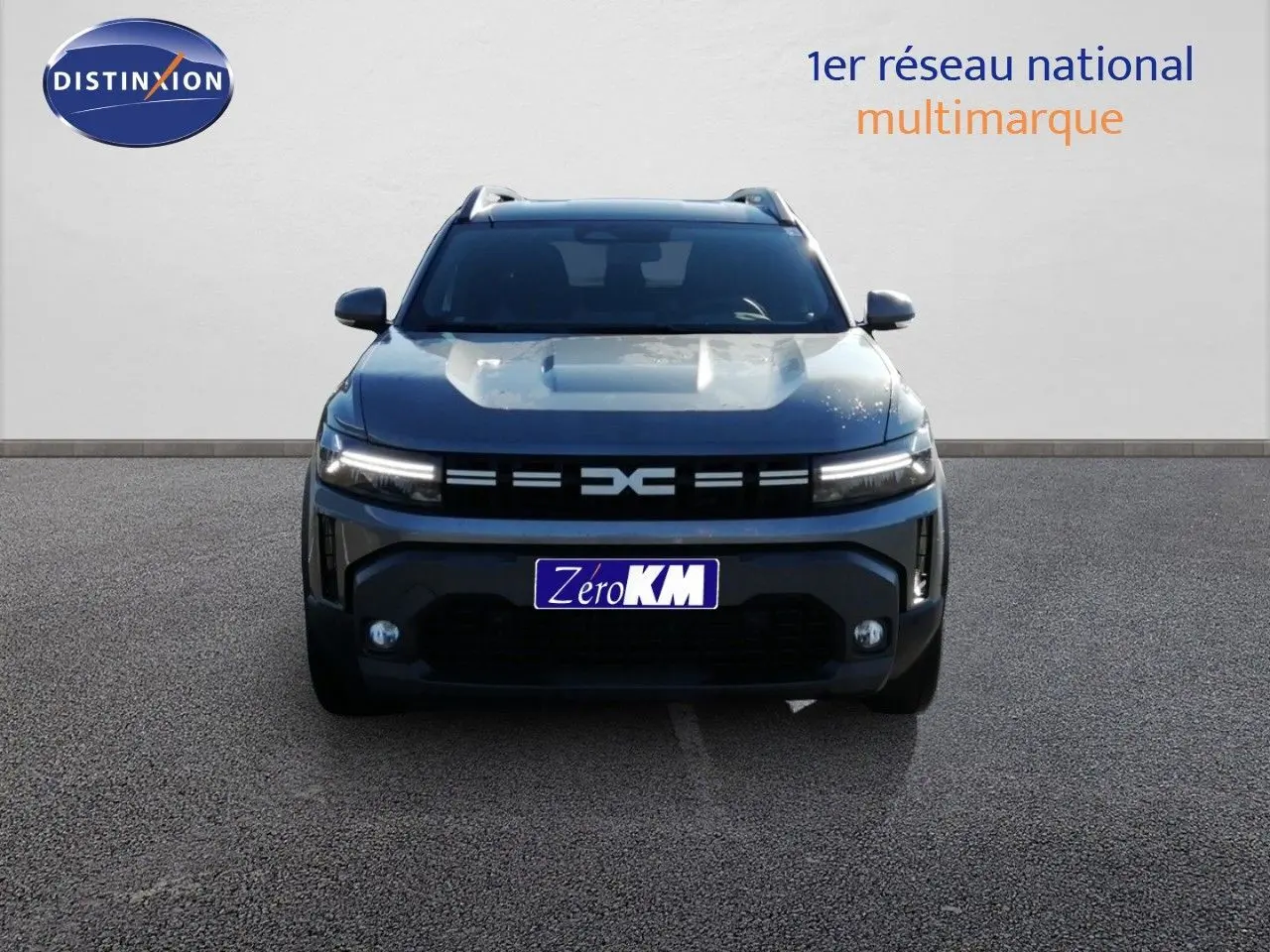 Vue de face du Dacia Duster gris schiste métal 2026 avec calandre noire et feux LED allumés sur fond clair.