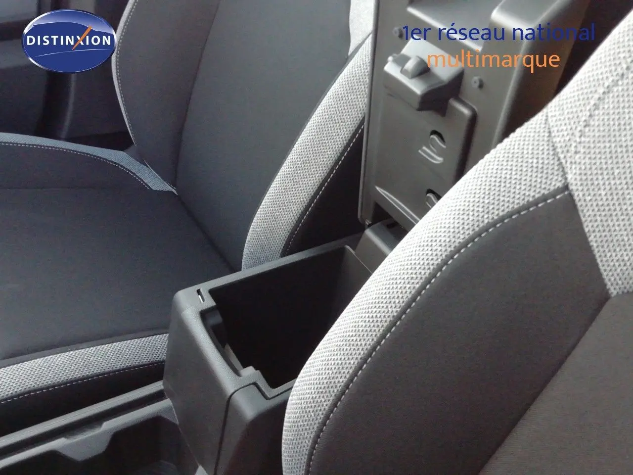 Détail intérieur montrant l'accoudoir central ouvert entre les sièges tissu gris clair et noir du Dacia Duster 2026.