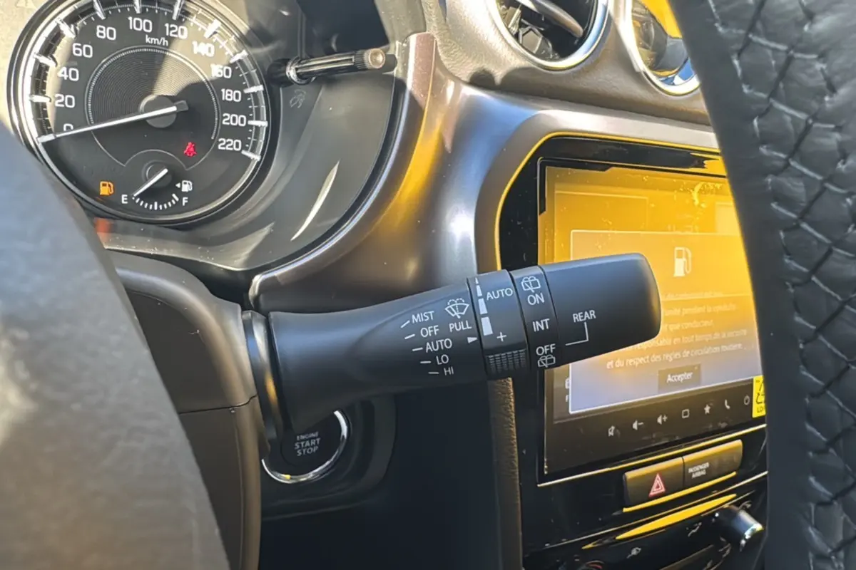 Détail intérieur du Suzuki Vitara 2025 montrant le commodo d’essuie-glace, le compteur et l’écran tactile sur fond noir.