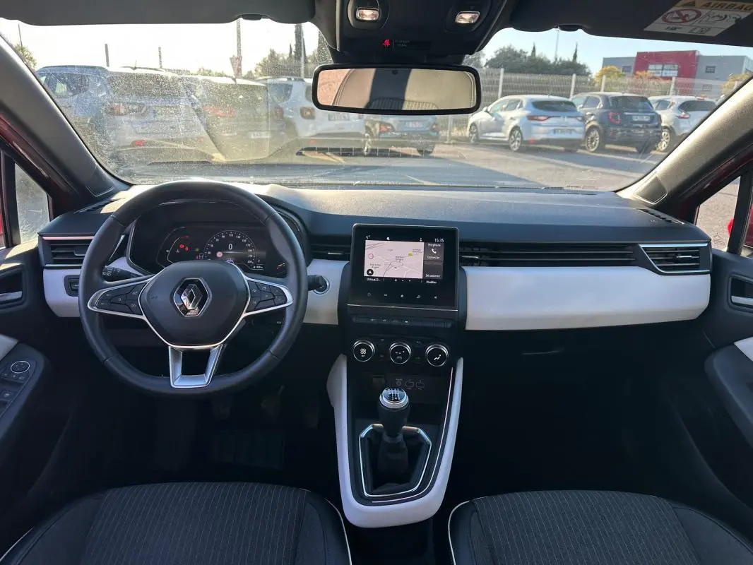 Vue intérieure avant de la Renault Clio rouge foncé 2021, volant cuir, écran tactile et levier de vitesse manuel visibles.