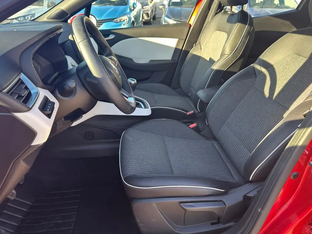 Vue intérieure côté conducteur de la Renault Clio rouge foncé, sièges tissu noir avec surpiqûres blanches et volant cuir.